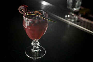 Wine glass with red nonalcoholic cocktail with blueberries and allspice, decorated with fresh sweet pastille