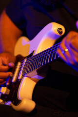 Guitarrista tocando sua guitarra branca em show com luz cenográfica de cor azul e amarelo.  
