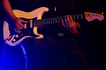 Guitarrista tocando sua guitarra branca em show com luz cenográfica de cor azul e amarelo.  