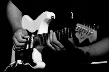 Guitarrista tocando sua guitarra branca em show em preto e branco.   - obrazy, fototapety, plakaty