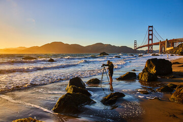 Photographer on Marshalls Beach capturing golden sunset with Golden Gate Bridge behind him