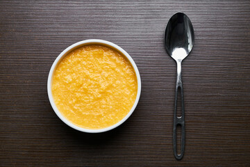 A bowl of pumpkin porridge with a silver spoon on a textured dark brown table - an appetizing blend...