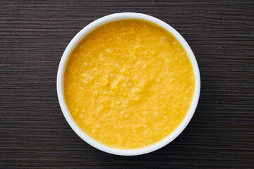 A bowl of pumpkin porridge on a textured dark brown table - an appetizing blend of Thanksgiving and healthy dining, embodying the essence of nourishing traditions. Top view.