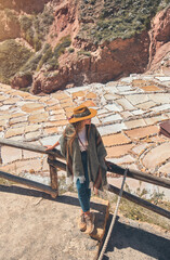 Aerial view Tourist with Traveler hipster girl in hat and poncho exploring Maras Salt Mines, Peru. Travel and wanderlust concept.