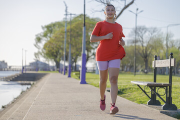 Latin girl in red t-shirt running along the river boardwalk at dawn.