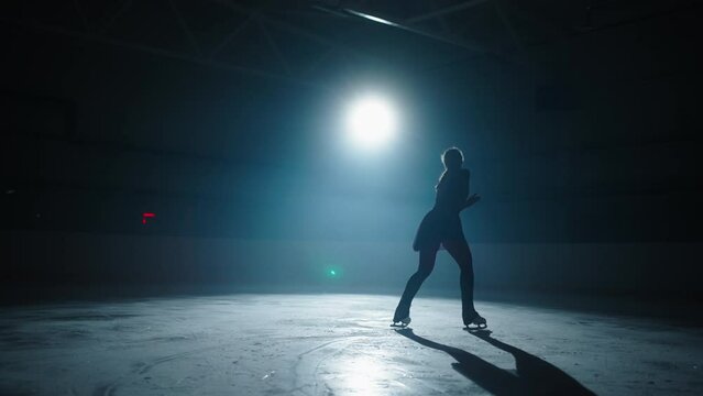 Cinematic Shot On Ice Rink With Professional Female Figure Skater Whirling On Ice In Darkness