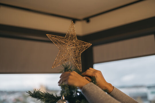 Cropped image of a woman's hands placing a shiny decorative star on the top of a Christmas tree.c
