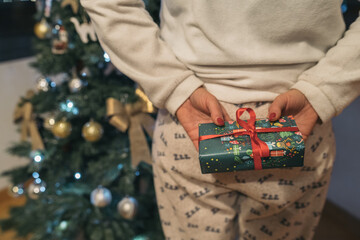 Woman hiding a Christmas gift behind her. Young girl in pajamas holding behind her back a present...