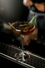 Glass of delicious cocktail decorated with banana leaf and ice cube standing on steel barstand