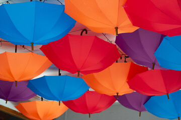Street photo. Multicolored umbrellas hang upside down. Decoration on ceiling. Red, orange, blue, purple color. Concept of rainbow, rain, rainy bad weather, style, cloudy day, festival, carnival, fair
