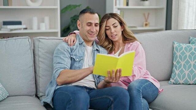 Man and woman couple reading book sitting on sof at home