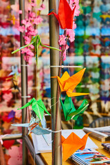 Close up of origami cranes with pink cherry blossoms behind and blurry flowers in background