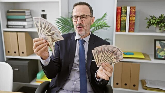 Hispanic, middle-age, grey-haired, suit-clad business worker ecstatically kissing banknotes in his office, instinctively smiling while basking in the joys of professional success.