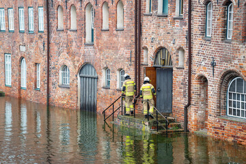 High water flooding the old town of Lubeck when the river Trave overflows its banks, specialists control water level and danger at a historic building of red brick architecture - 665239016