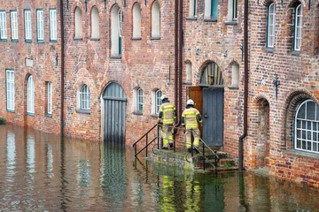 Foto op Aluminium High water flooding the old town of Lubeck when the river Trave overflows its banks, specialists control water level and danger at a historic building of red brick architecture © Maren Winter