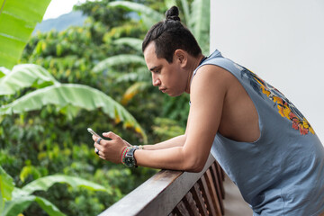 Naklejka na ściany i meble Man standing on a balcony looking at his cell phone