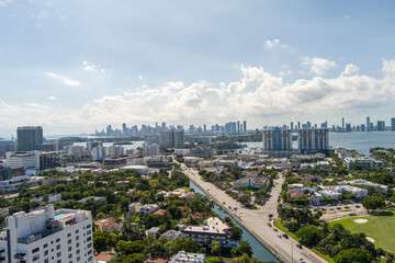 aerial shot of the hotels, condos and skyscrapers in the city skyline with blue ocean water and lush green trees and grass, blue sky and clouds in Miami Beach Florida USA