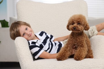 Little child with cute puppy in armchair indoors. Lovely pet