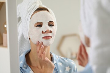 Young woman with face mask looking into mirror indoors. Spa treatments