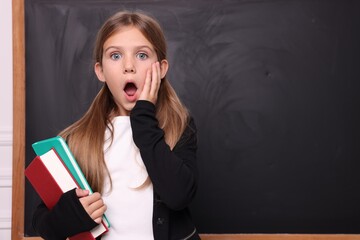 Shocked schoolgirl with books near blackboard. Space for text
