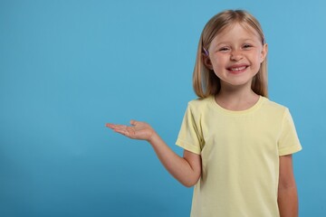 Special promotion. Little girl showing something on light blue background. Space for text