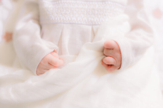 A close-up of sweet newborn baby hands curled up on her white dress.