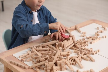 Little boy playing with wooden blocks at table indoors, closeup. Child's toy