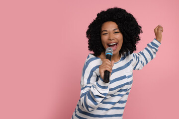 Fototapeta na wymiar Beautiful woman with microphone singing on pink background, space for text