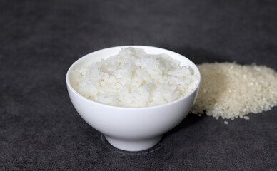 Raw rice and cooked rice. White rice bowl on a dark background.
