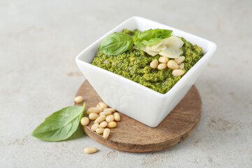 Bowl with delicious pesto sauce, cheese, pine nuts and basil leaves on light table, closeup