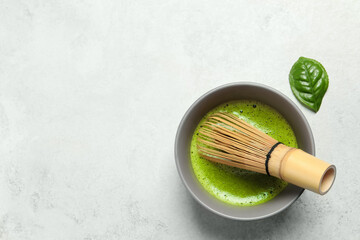 Cup of fresh green matcha tea with bamboo whisk on light grey table, top view. Space for text