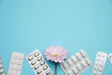 Keuken spatwand met foto Many gynecological pills and gerbera flower on light blue background, flat lay. Space for text © New Africa