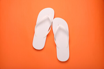 Stylish white flip flops on orange background, top view