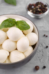 Tasty mozzarella balls and basil leaves in bowl on grey table, above view