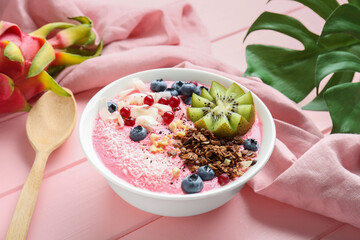 Tasty smoothie bowl with fresh kiwi fruit, berries and granola on pink wooden table