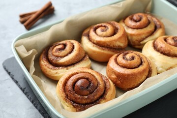 Baking dish with tasty cinnamon rolls on grey table, closeup