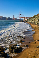 Waves crashing against beach with rocky shoreline and Golden Gate Bridge