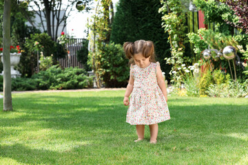 Cute little girl walking on green grass in park