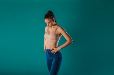 Confident fit girl poses in a studio, showcasing her muscular physique and fitness motivation. With a turquoise background, this young woman inspires with her powerful presence and impressive results.