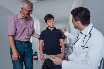 Obraz premium In a medical office, doctors discuss diagnosis and treatment options with a child patient and concerned grandfather. Clinical outcomes and healthcare solutions are explored.