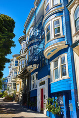 Obraz premium Side view row of houses with bright blue paint and fire escape ladders and a red front door