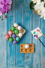 Multicolored easter eggs on blue table with paint brushes and paint