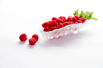 Raspberries and mint leaves in glass dish with a white background