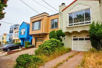 Overgrown with weeds around front entrance to garage door of first house in row of homes