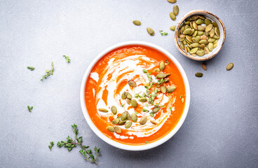 Autumn slow comfort food. Pumpkin soup puree with seeds, coconut cream and thyme.. Healthy vegetarian food. White soup bowl on gray table background. Top view - obrazy, fototapety, plakaty