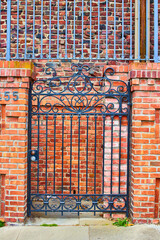 Black gate with red brick wall behind it and pillars closing off unseen residence in optical...