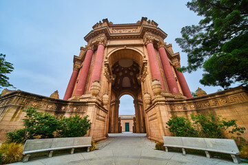 Fototapeta premium Stone benches leading into Palace of Fine Arts open air rotunda under light blue sky with green tree