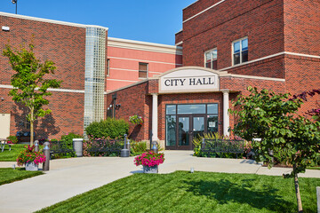City hall sign over public entrance with flowers on sidewalk and seating