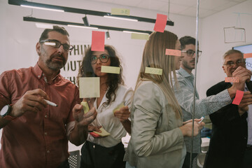 Business colleagues writing sticky notes on the window while standing at the co working space