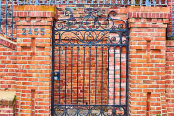 Black gate with red brick wall pillars and optical illusion of a wall behind it